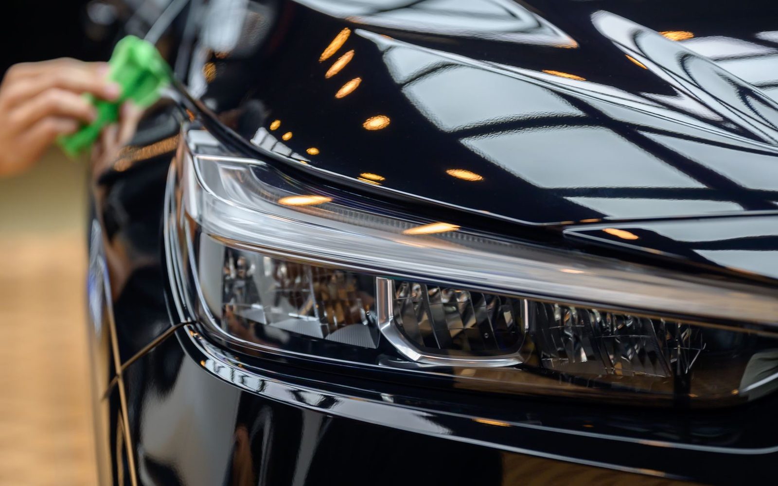 Detailer hand-finishing a polished black headlight and fender under warm shop lights